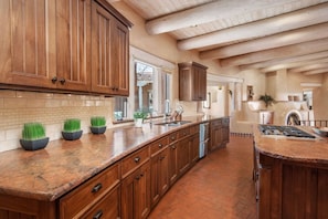 A spacious kitchen with wooden cabinets, a large island, and a brick floor.