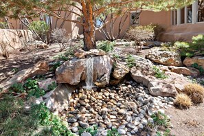 A landscaped garden with a waterfall, rocks, and a tree.