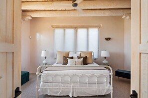 A bedroom with a metal bed frame, two bedside lamps, a window with blinds, and a wooden ceiling.