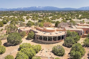 A large, circular building with a central courtyard surrounded by smaller structures, set in a desert landscape with distant mountains.