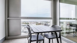 Un balcon moderne, doté d’une table et de chaises, qui offre une vue sur la ville grâce à de grandes fenêtres.