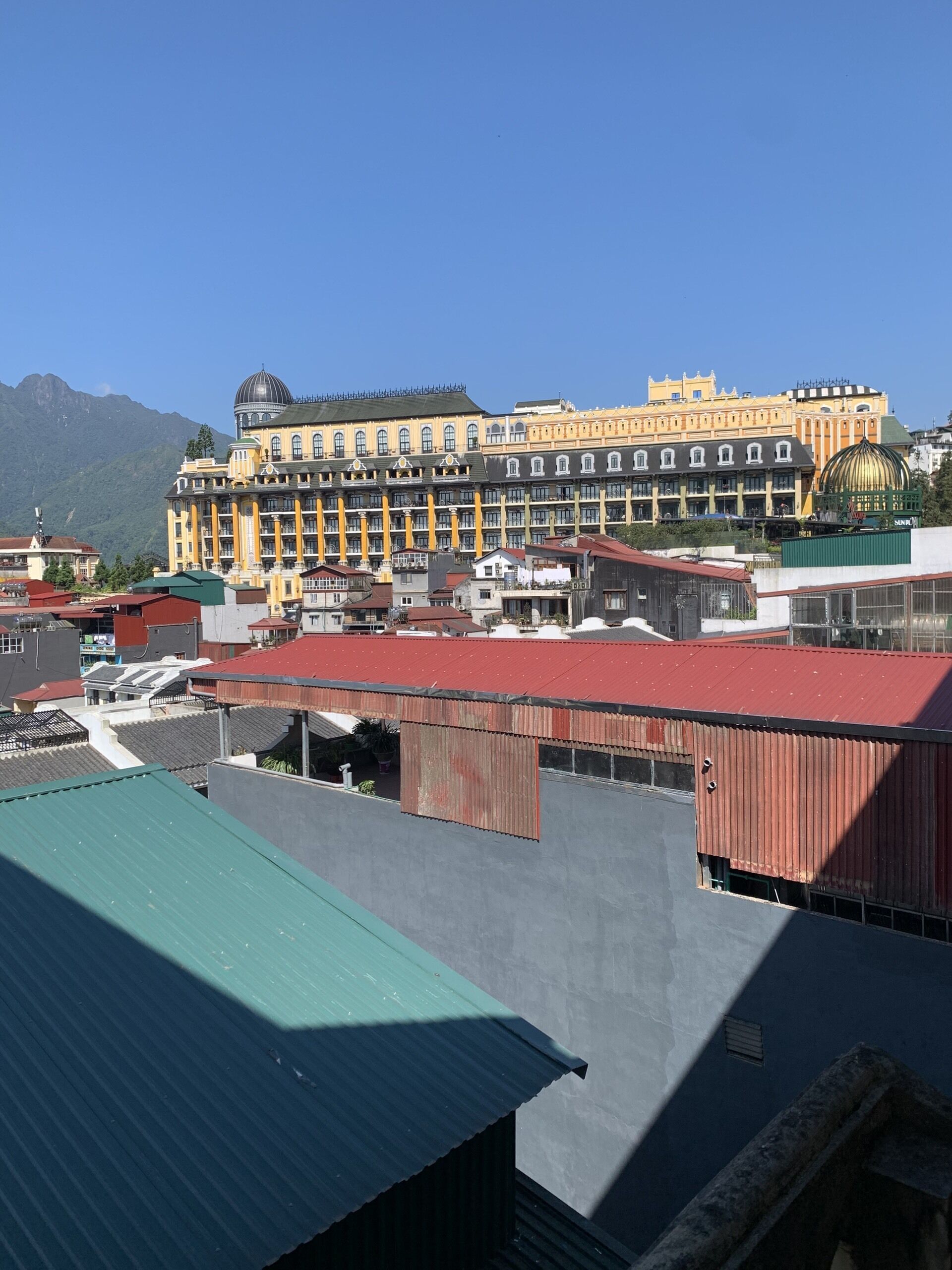 Un edificio grande de varios pisos con una cúpula destacada y arquitectura clásica, rodeado de otros edificios y montañas al fondo.