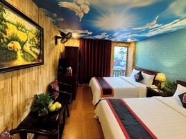 A hotel room with a mural, two beds, a desk, a chair, a plant, and a window with a view.