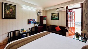 A hotel room with a bed, a desk, a chair, a sofa, a TV, and a window with a view.