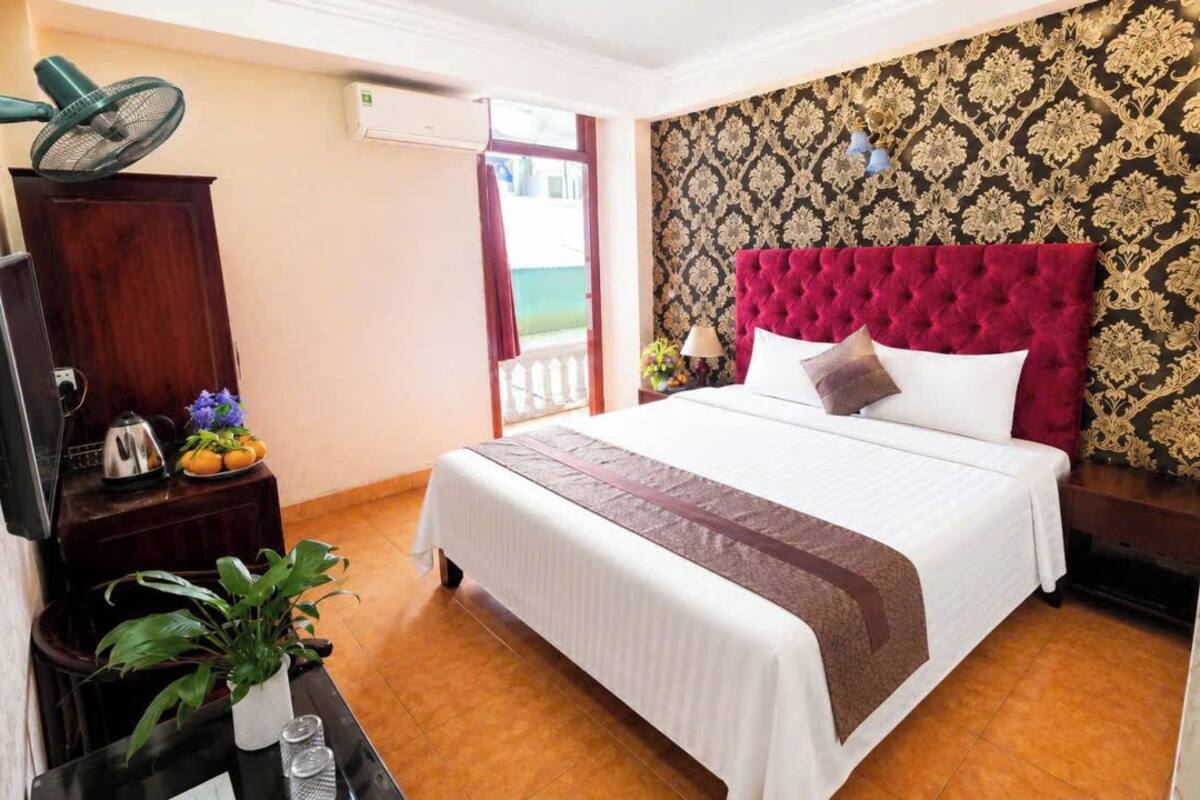 A hotel room with a bed, a TV, a plant, and a fan.