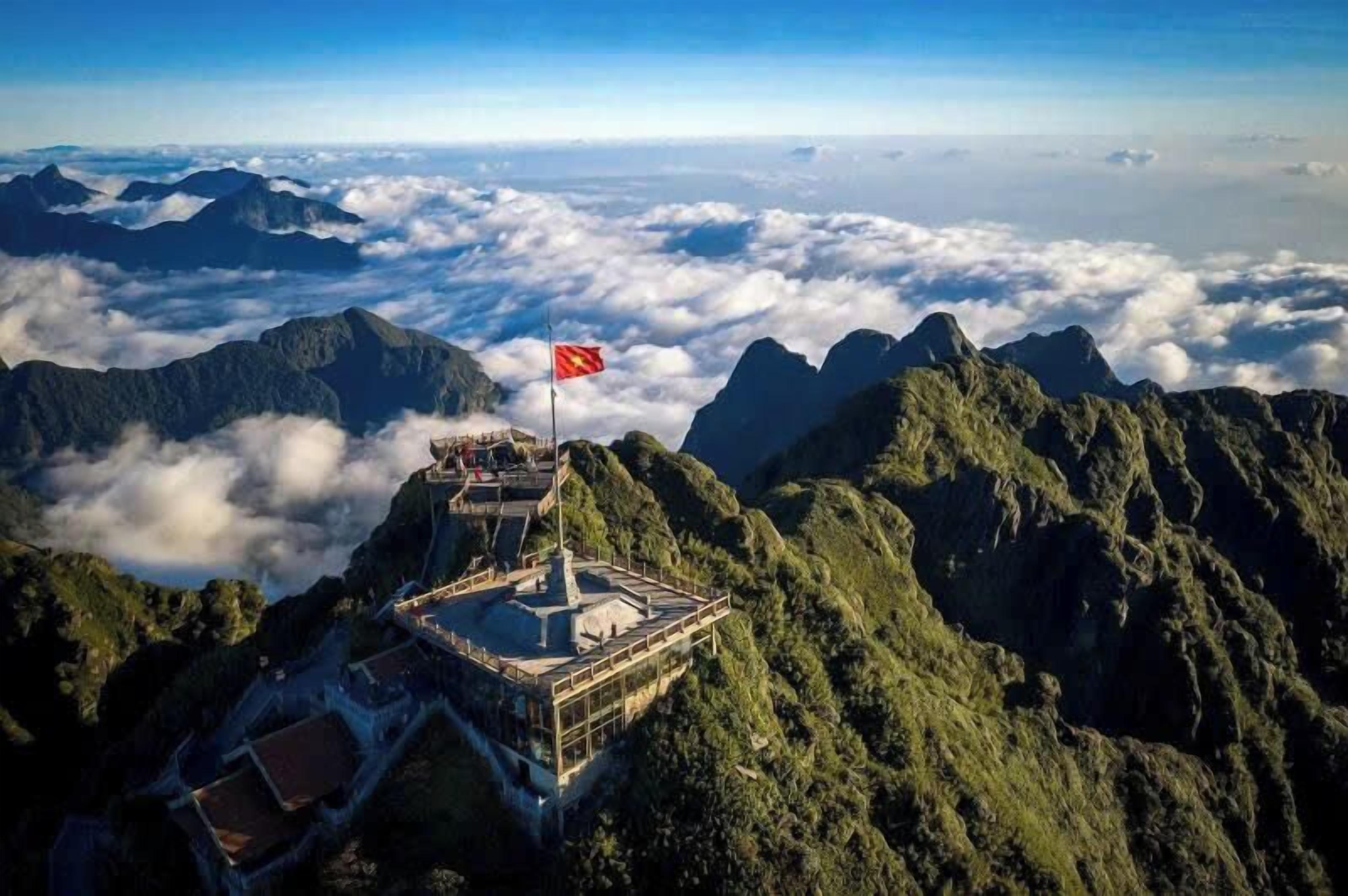 Un punto panorámico de gran altura con una bandera en la cima de una montaña, rodeado de nubes y terreno accidentado.