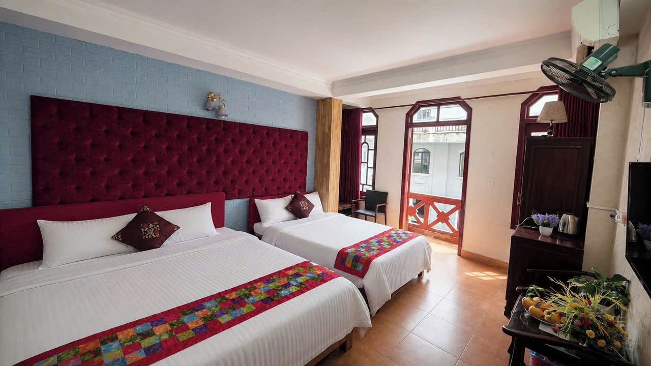 Een hotelkamer met twee bedden, een rode hoofdbord, een balkon met uitzicht en een ventilator.