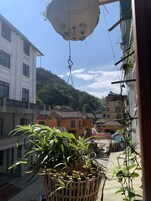 Un balcón con una maceta colgante, edificios al fondo y un cielo despejado.