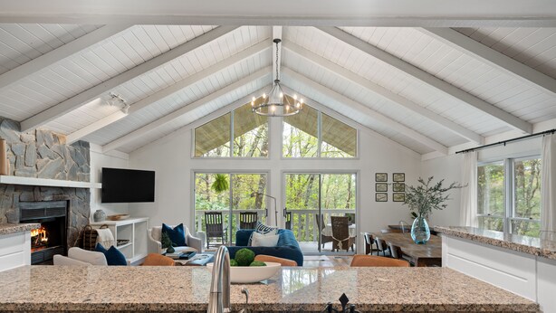 A spacious interior with a high ceiling, a stone fireplace, a kitchen island, and large windows offering a view of the outdoors. - Cozy Cottage in Highland Falls Country Club Just 2.5 miles to Downtown Highlands (Highlands)