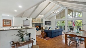 A spacious living area with a fireplace, a dining table, and a large window overlooking a deck. - Cozy Cottage in Highland Falls Country Club Just 2.5 miles to Downtown Highlands (Highlands)