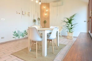 A dining area with a white table, chairs, hanging lights, and potted plants. - Central View Boutique (Cesena)