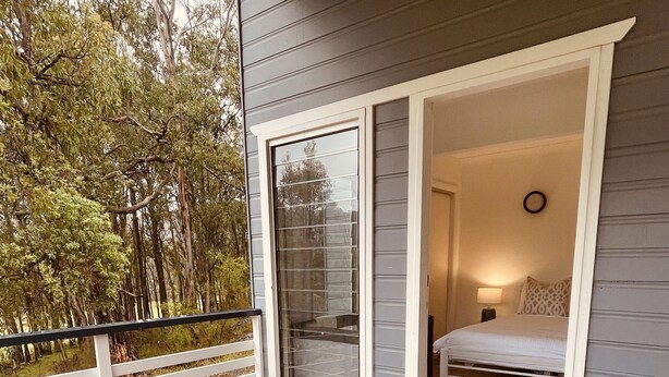 Eine Holzterrasse mit zwei Korbstühlen und einer Glastür, die zu einem Schlafzimmer mit Bett und Nachttisch führt.