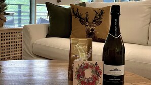 Eine Flasche Petersson House Sekt, eine Lindt Schokoladentafel und eine Grußkarte auf einem Holztisch in einem Raum mit einem weißen Sofa und einem Deer Kissen.