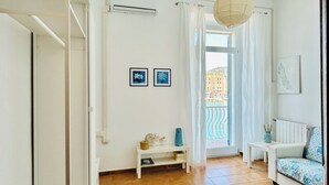 Ein geräumiges Wohnzimmer mit großem Fenster, einem weißen Sofa, einem kleinen Tisch und einer Hängeleuchte.