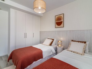Ett sovrum med två sängar, en garderob, en hängande lampa och ett konstverk som hänger på väggen.