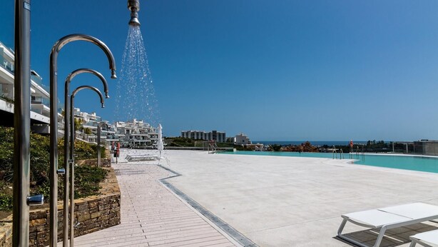 Un espace aménagé au bord d’une piscine, avec un ciel d’un bleu limpide, une piscine et une rangée de structures métalliques.