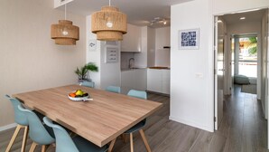 Une cuisine moderne avec des meubles blancs, une table à manger en bois et des chaises bleues. Deux suspensions en osier sont suspendues au-dessus de la table.