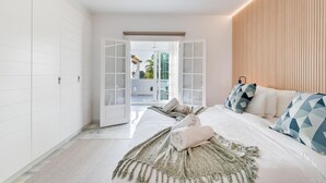 Un dormitorio moderno con una cama grande, cabecera de madera y vistas al exterior a través de una puerta abierta.