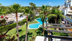 Zona de piscina con palmeras, cielo azul despejado y vistas de edificios circundantes.