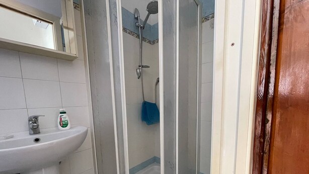 Un baño con lavamanos blanco, cabina de ducha y una alfombra de baño azul.