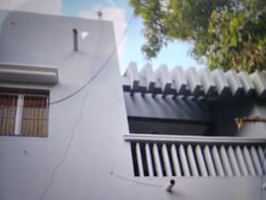 Um edifício com fachada branca, uma janela com grade de metal e uma árvore ao fundo.
