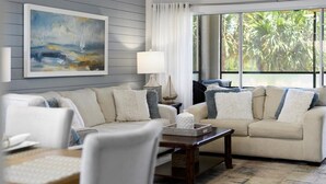 Ein Wohnzimmer mit einem beigefarbenen Sofa, einem Holztisch und einem Bild an der Wand.