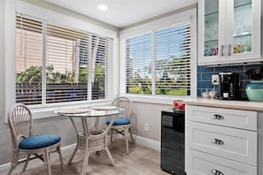 Une cuisine avec un coin repas, des meubles blancs et une vue sur la verdure.