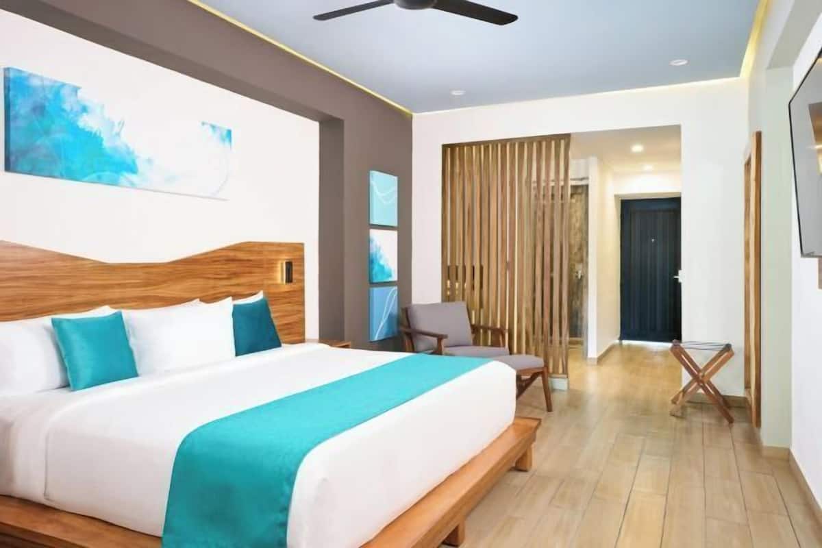 Habitación de hotel moderna con una cama grande, cabecero de madera y vista al pasillo.