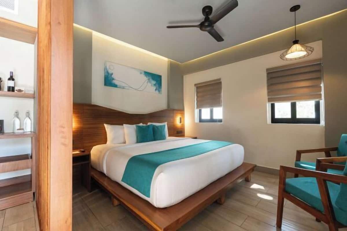 Habitación de hotel moderna con cama de madera, ventilador de techo, una obra de arte en la pared y una ventana con persianas.