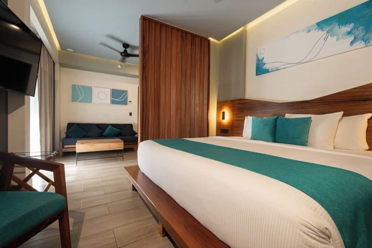 Una habitación de hotel con una cama grande, un cabecero de madera, un sofá, un televisor y un ventilador de techo.