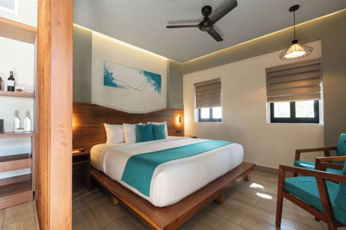 Habitación de hotel moderna con cama de madera, ventilador de techo, una obra de arte en la pared y una ventana con persianas.