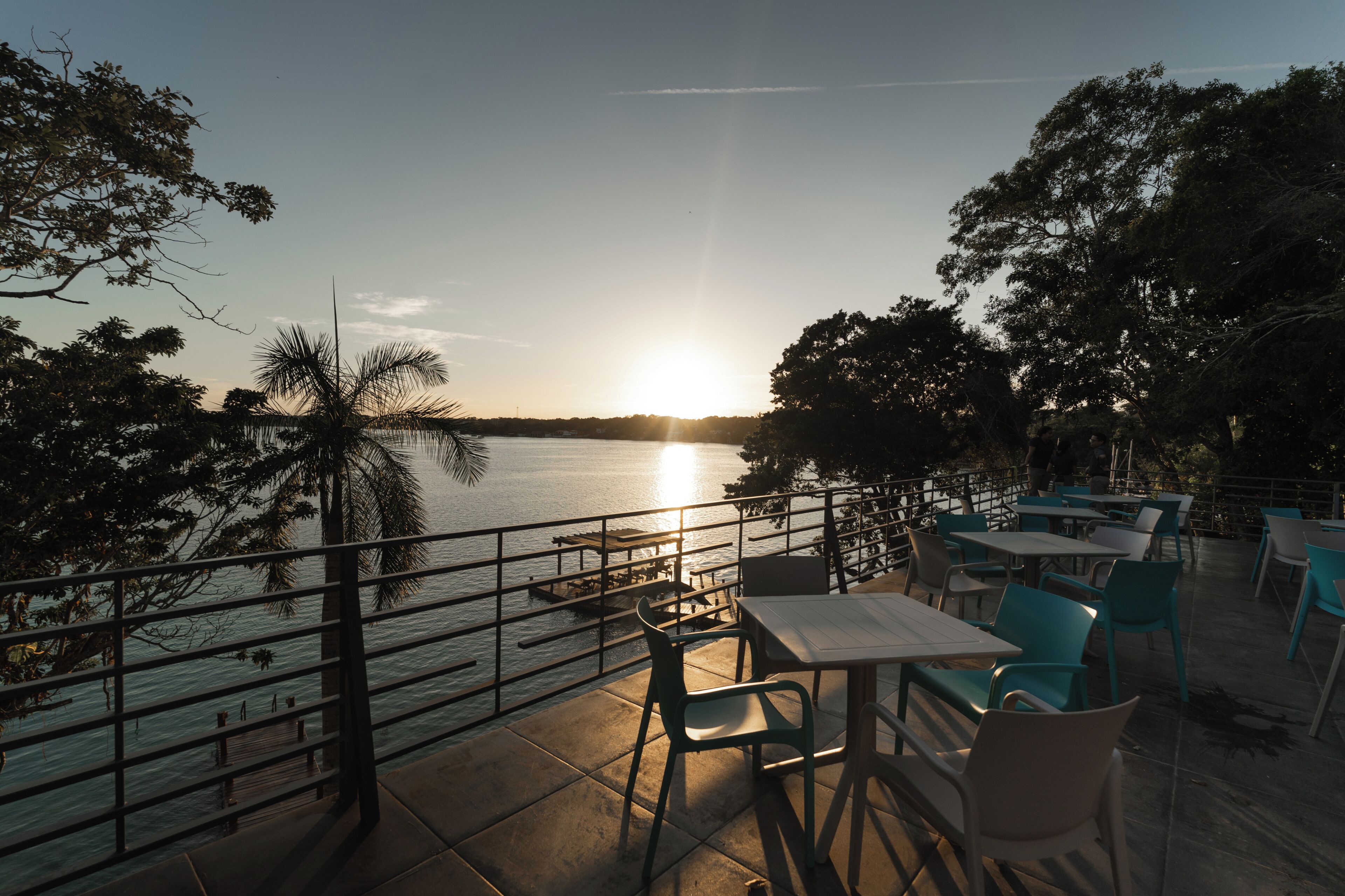 A terrace with tables and chairs overlooking a body of water at sunset.