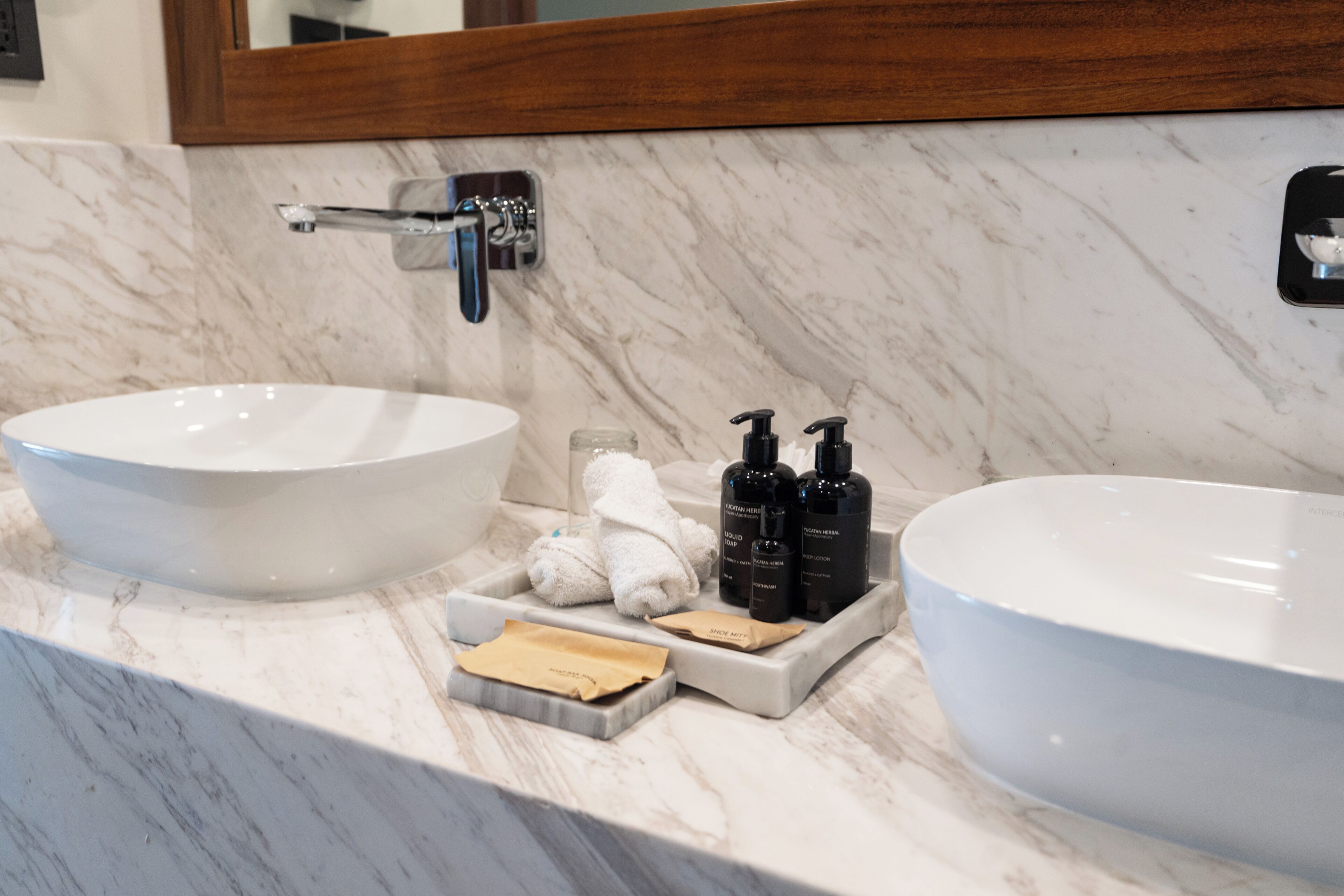 A bathroom with a marble countertop, two sinks, a mirror, and toiletries.