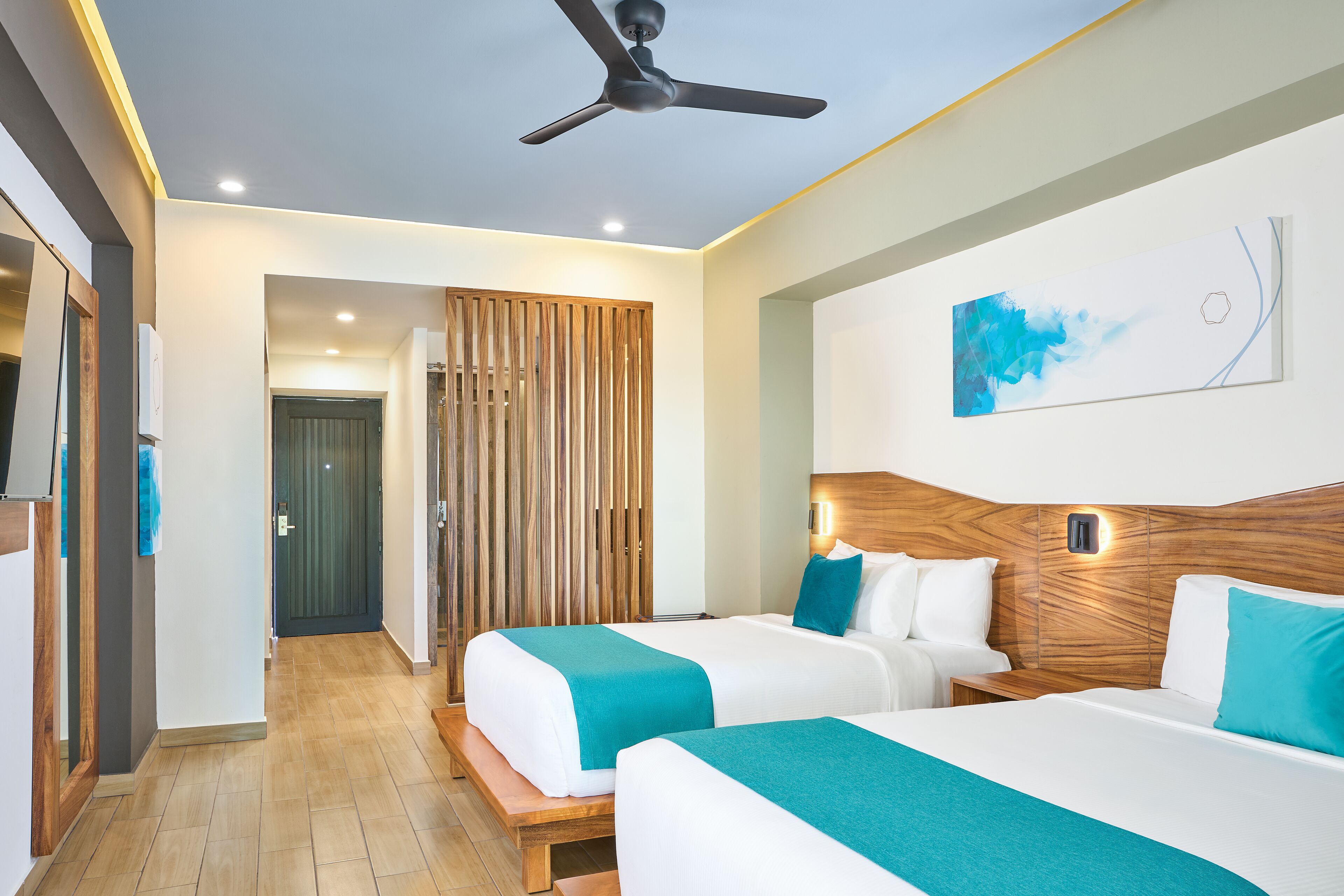 A hotel room with two beds, a ceiling fan, a wooden headboard, and a painting on the wall.