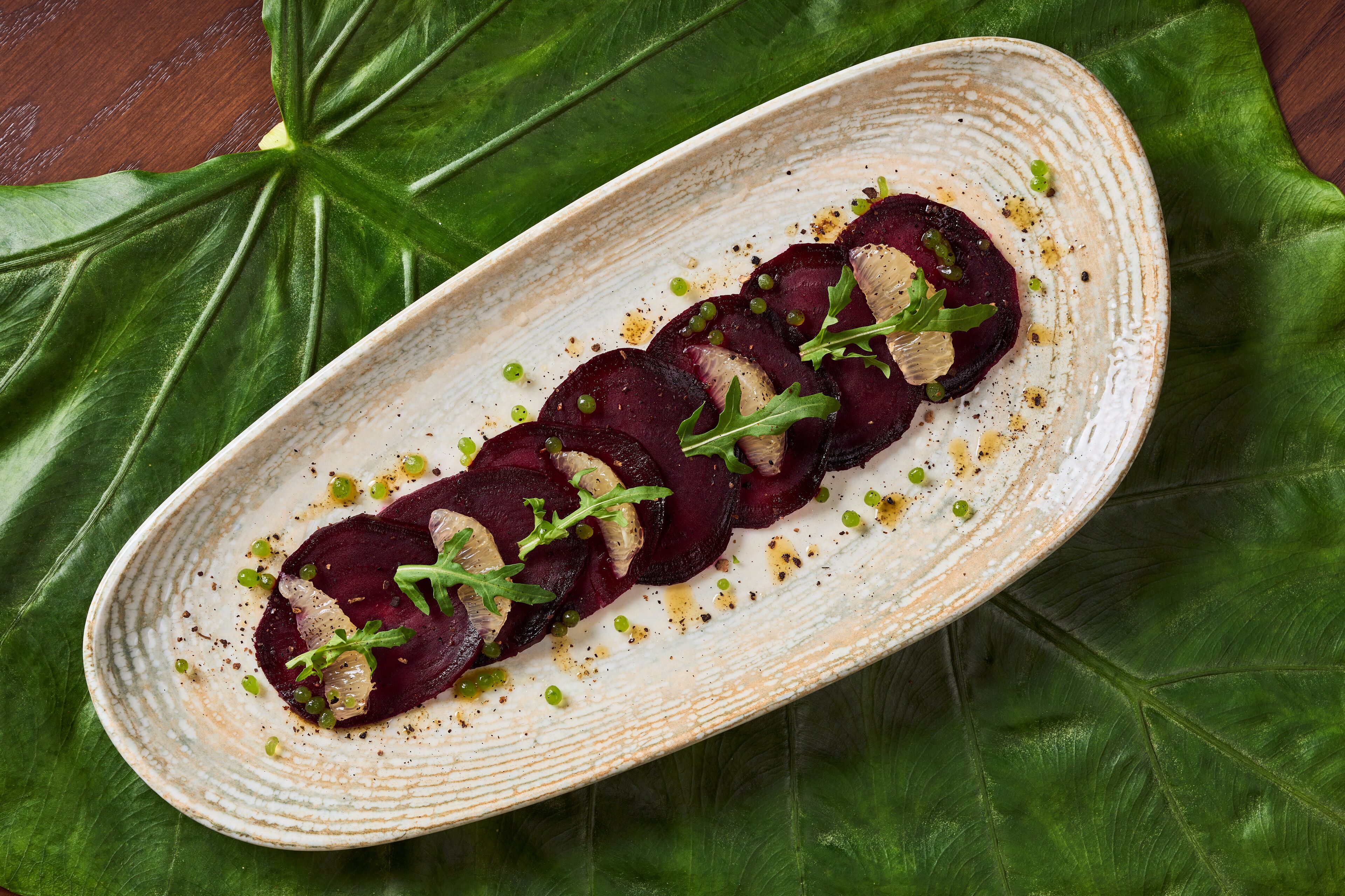 A plate of sliced beets garnished with greens and microgreens, placed on a textured ceramic plate.