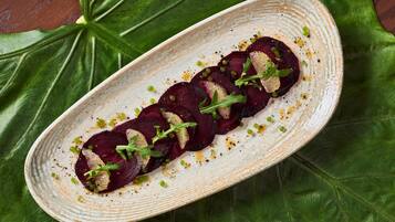 A plate of sliced beets garnished with greens and microgreens, placed on a textured ceramic plate.
