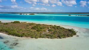 Luchtbeeld van een tropisch eiland met helder turquoise water, een zandstrand en weelderige begroeiing.