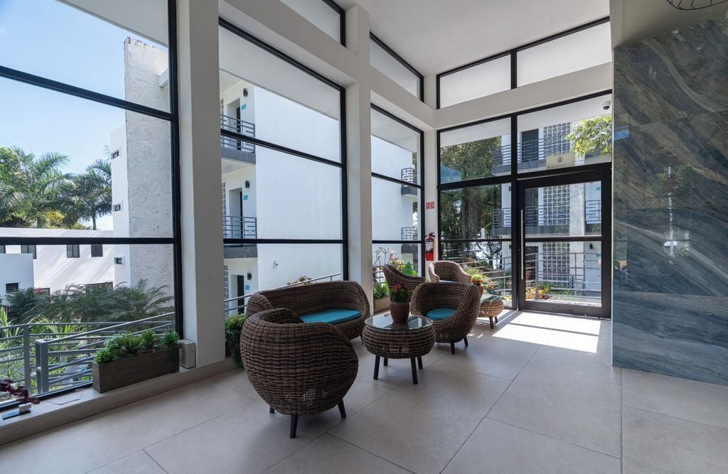 A modern balcony with wicker furniture, large windows, and a view of surrounding buildings.