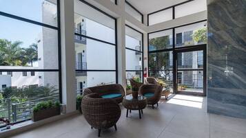 A modern balcony with wicker furniture, large windows, and a view of surrounding buildings.