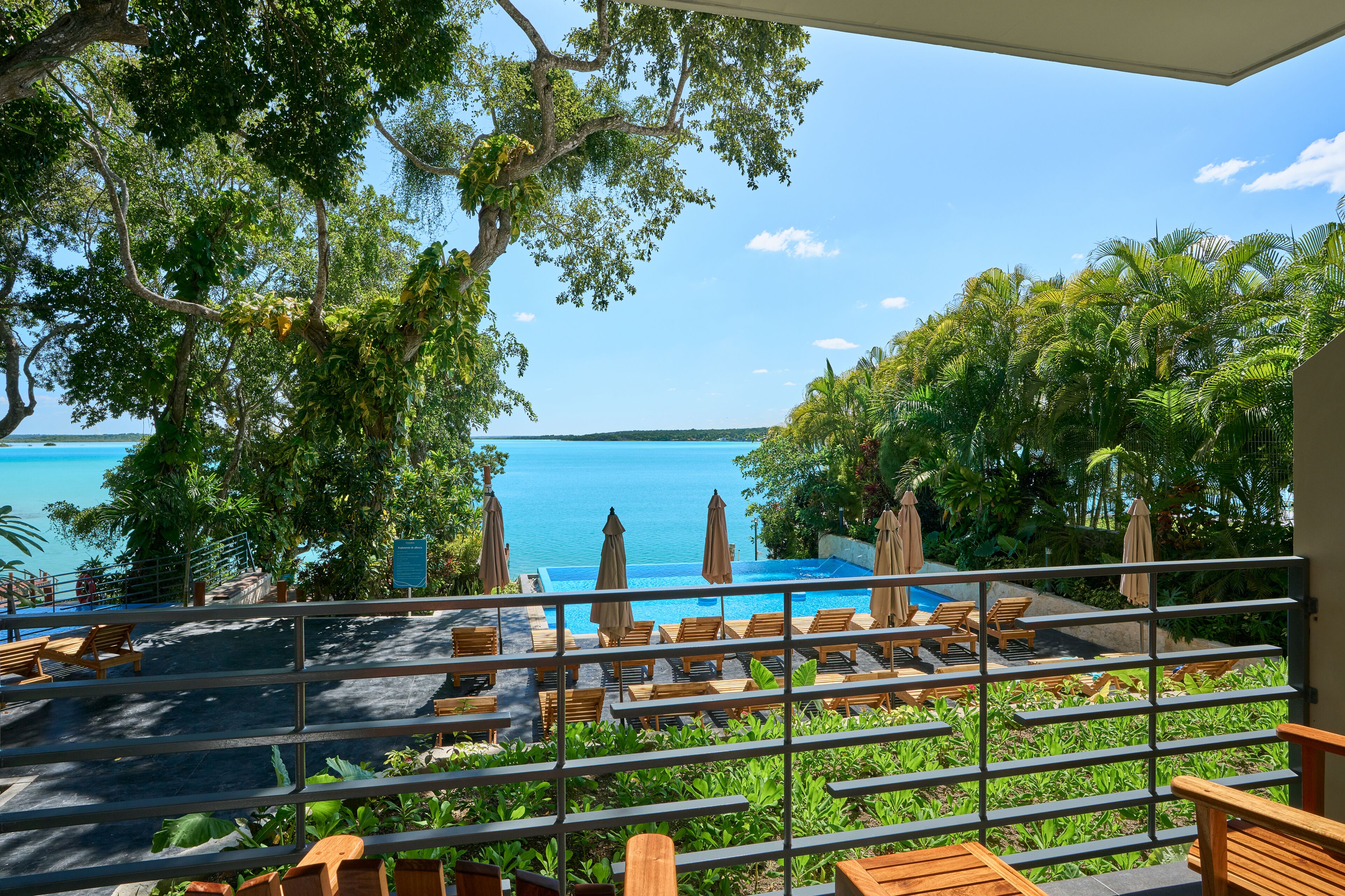A poolside area with lounge chairs and umbrellas, overlooking a clear blue sea.