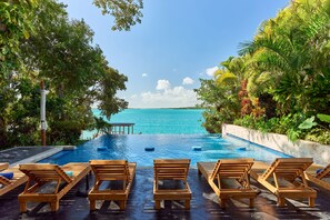 Un espace aménagé au bord de la piscine, avec des chaises longues en bois et une vue sur l’océan.