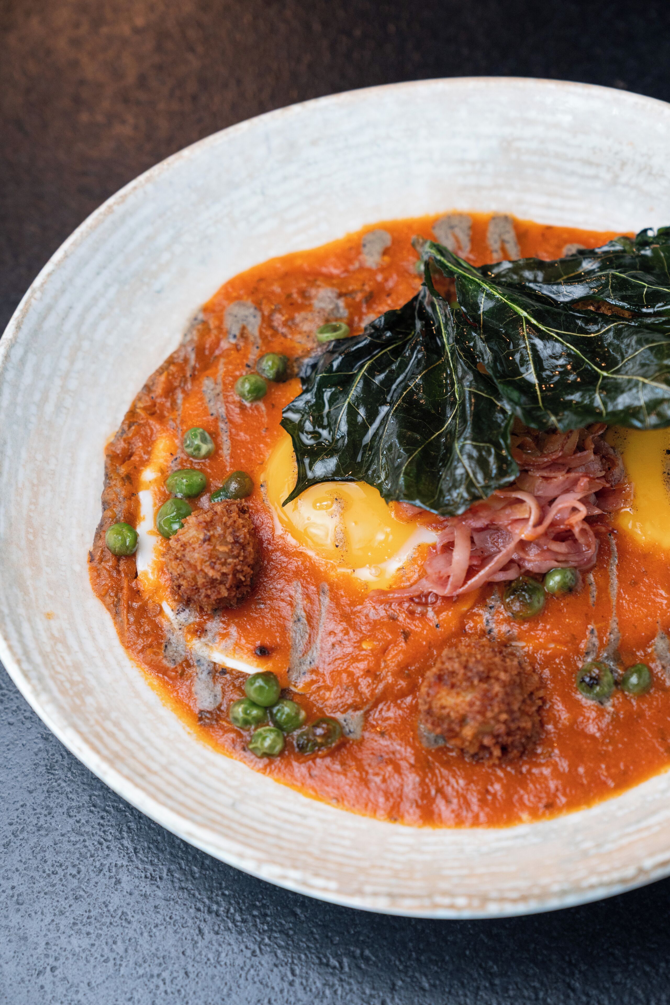 A bowl of soup with greens, peas, and meatballs.