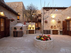 Un patio con muros de piedra, una fogata en el centro y cestas de flores colgantes.