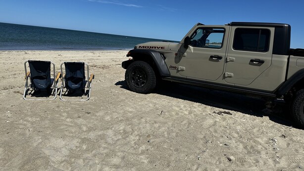 A beige Jeep Wrangler parked on a sandy beach with two beach chairs. - Private Modern Bedroom In a Central Location (Nantucket)