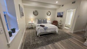 A bedroom with a large bed, two bedside tables, a nightstand, a chair, a small table with a lamp, and a mirror on the wall. - Private Modern Bedroom In a Central Location (Nantucket)