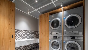 A laundry room with three stacked front-loading washing machines, a patterned tile floor, and a wooden bench. - Shanghai Hongqiao NECC Glory Hotel (Shanghai)