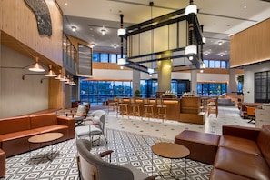 A modern lobby with a high ceiling, multiple seating areas, and large windows providing natural light.
