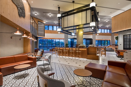 A modern lobby with a high ceiling, multiple seating areas, and large windows providing natural light.