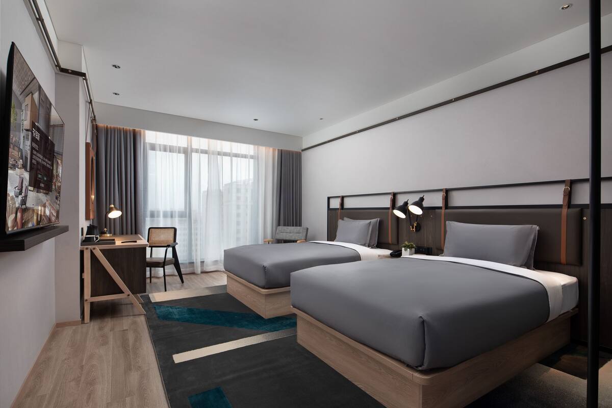 A modern hotel room with two beds, a desk, and a chair.