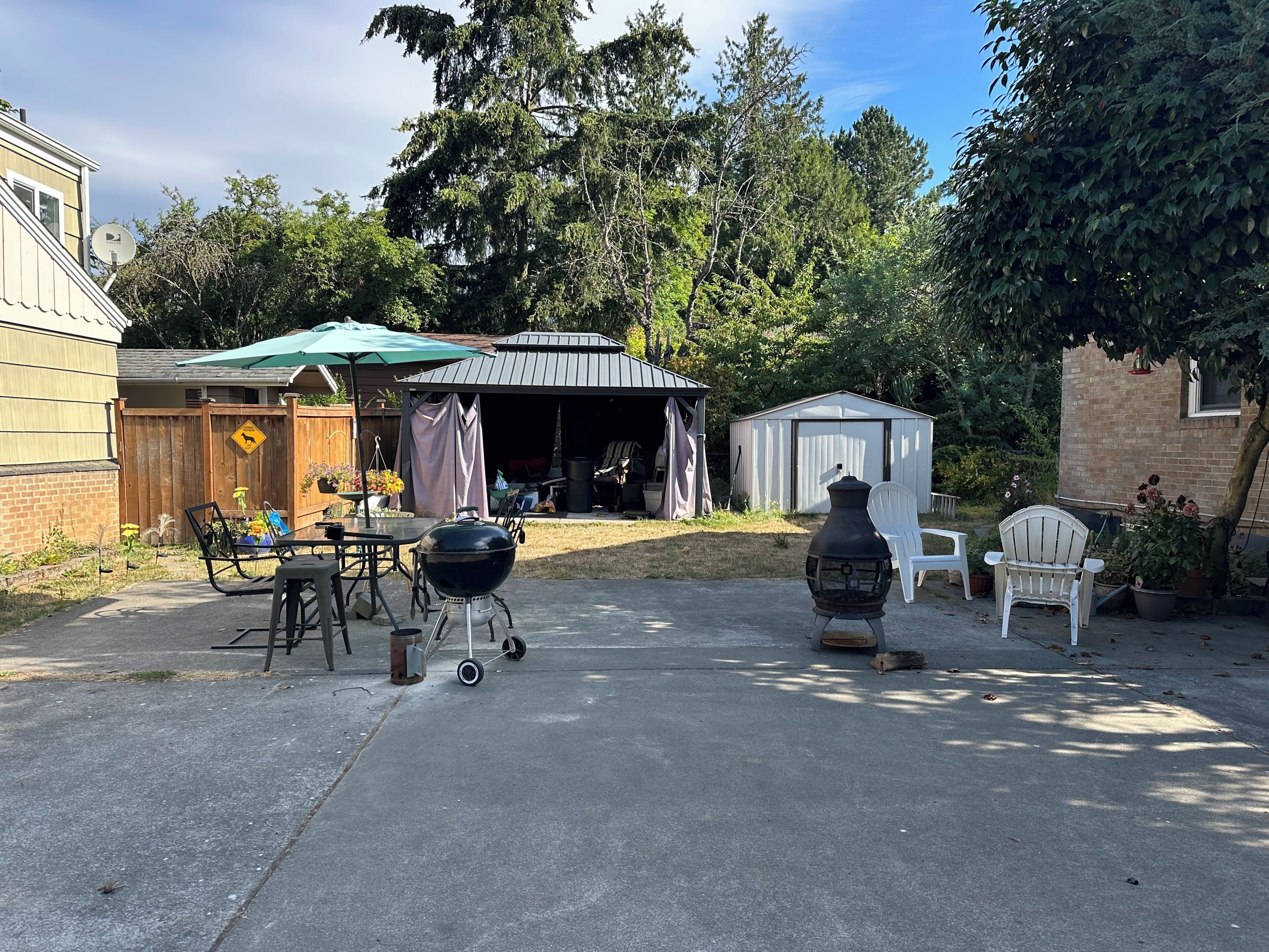 Ein Garten mit Grill, Gartenmöbeln, einem Schuppen und einer überdachten Terrasse.